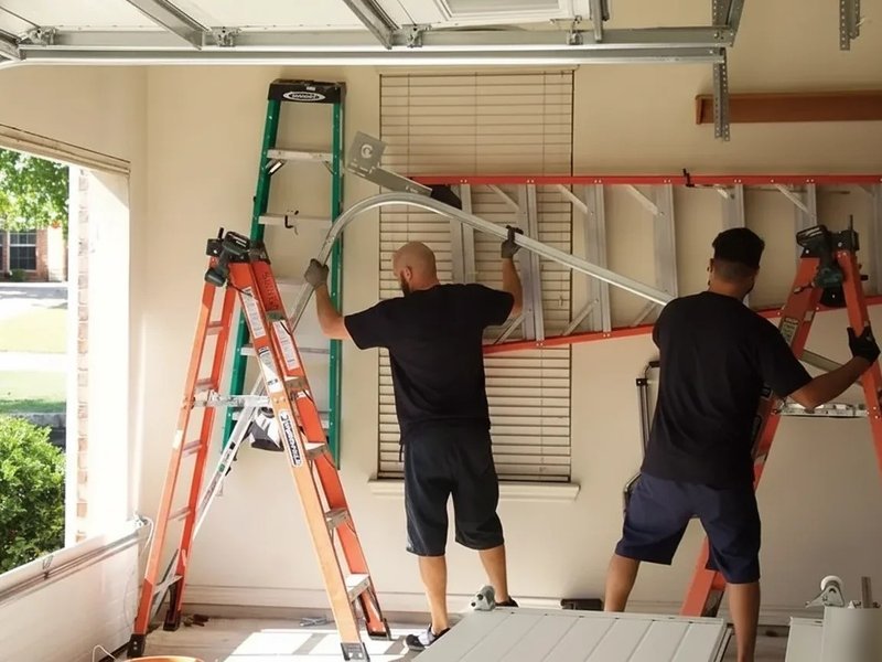 Two technicians on ladders working at upper door hardware